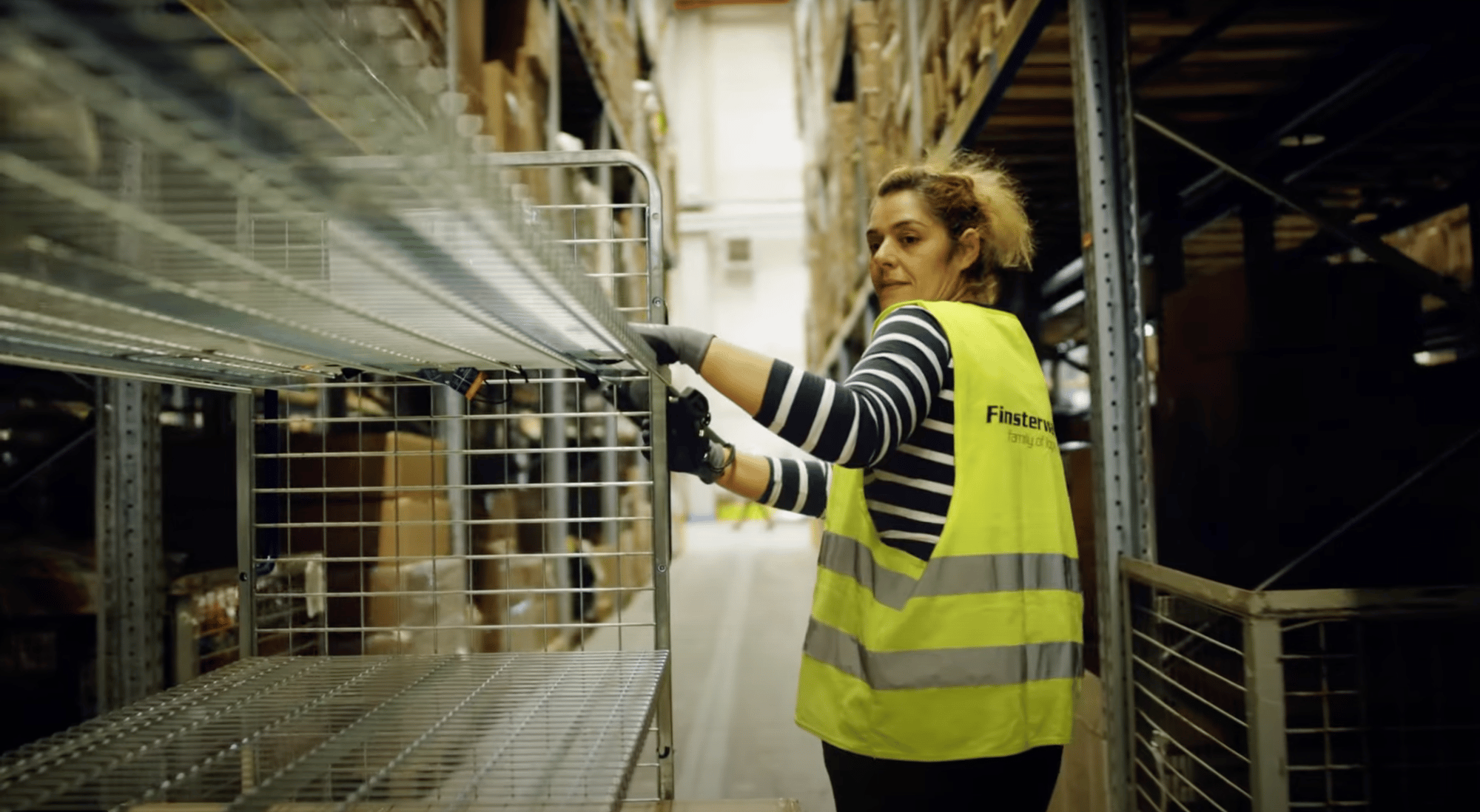 Eine Mitarbeiterin steht in einen Hochregal Lager